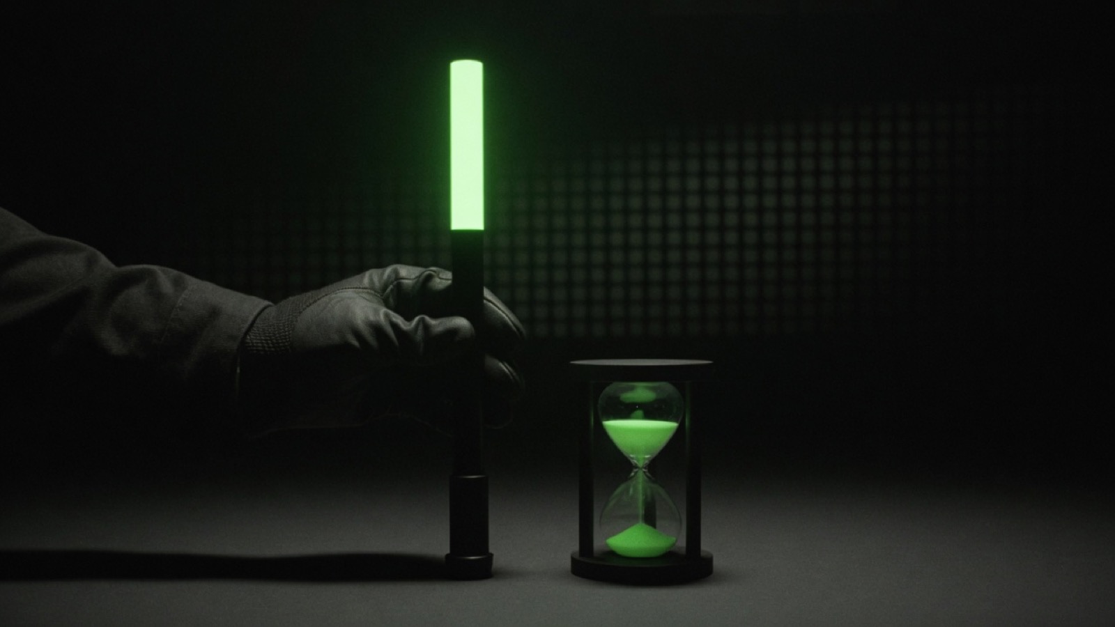 A gloved hand holds a fuel dipstick whose upper half glows green, beside an hourglass of green sand.
