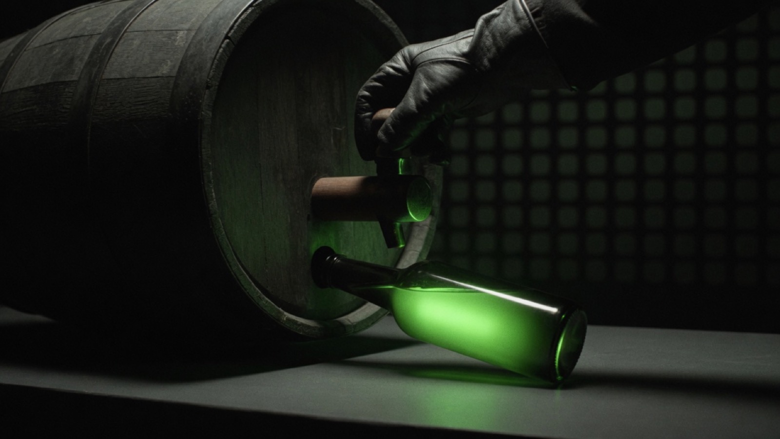 A gloved hand turns the tap of a dark keg while a bottle of green light lies on the table.