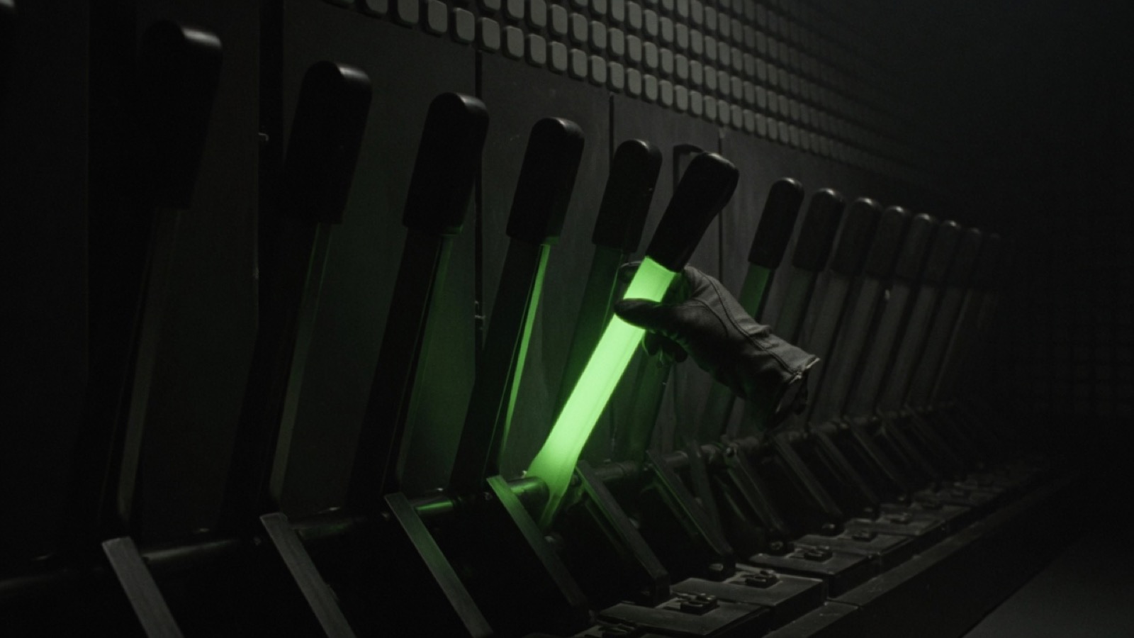 A gloved hand pulls the one glowing lever in a long row of dark levers.