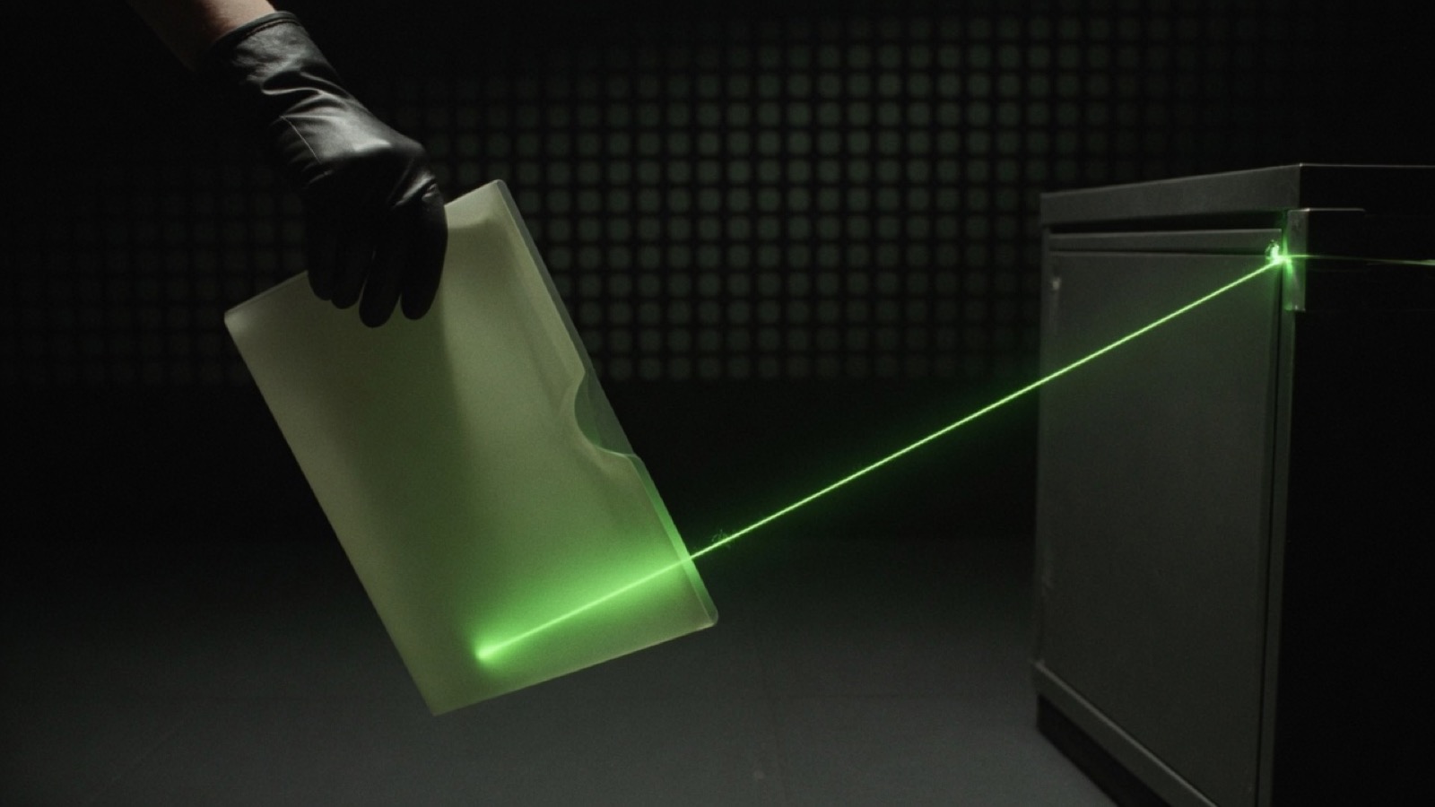 A gloved hand holds a translucent folder while a taut green line runs from it to a dark filing cabinet.